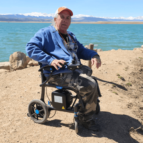 Senior man relaxing outdoors by a mountain lake in an All Star electric wheelchair