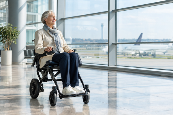 Older traveler using a lightweight electric wheelchair in a bright modern airport terminal