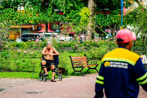 Senior man seated in a wheelchair on a park path on a sunny day, illustrating the electric wheelchair vs mobility scooter decision for seniors