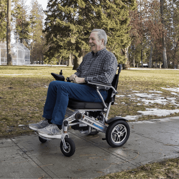 Older man smiling outdoors in a park while using an All Star electric wheelchair, enjoying the freedom to get out again
